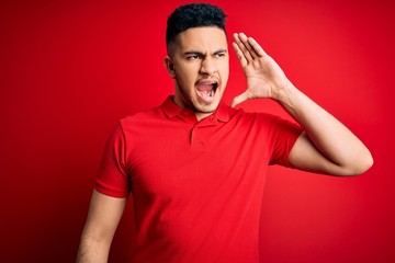 Young handsome man wearing red casual polo standing over isolated background shouting and screaming loud to side with hand on mouth. Communication concept.