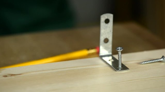 Close-up. A carpenter uses an electric screwdriver to tighten the screws in a wooden board.