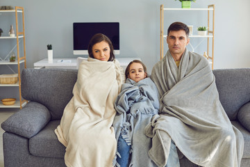 Sick family with a plaid sitting on a sofa looking at the camera with fever at home waiting for a doctor.