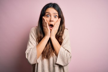 Young beautiful brunette woman wearing casual sweater standing over pink background afraid and shocked, surprise and amazed expression with hands on face