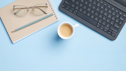 Home office desk with laptop computer, cup of coffee, paper notebook, glasses, pencil on blue background. Minimal style feminine workspace, business and education concept. Flat lay, top view