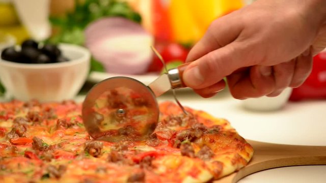 A man cuts pizza with a special knife. Pizza lies on a cutting board. 