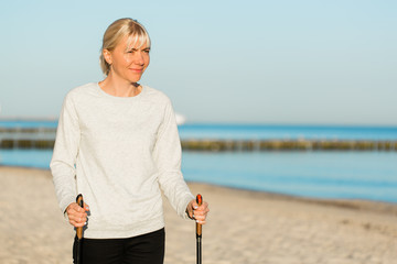 Pretty young woman resting after nordic walking on the beach. Healthy sport life concept