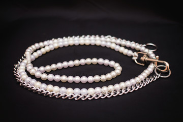 Beautiful ring made of white and beige pearls. Leash for a dog on a black background.