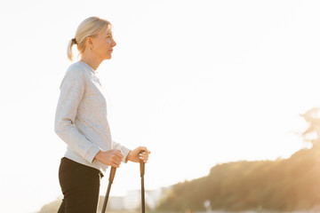 Pretty young woman resting after nordic walking on the beach. Healthy sport life concept