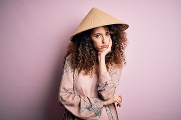 Young beautiful woman with curly hair and piercing wearing traditional asian conical hat thinking looking tired and bored with depression problems with crossed arms.