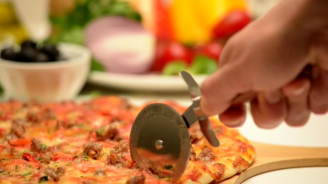 Pizza lies on a cutting board. A man cuts pizza with a special knife.