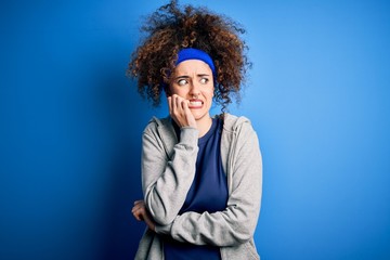 Young beautiful sportswoman with curly hair and piercing standing wearing sportswear looking...