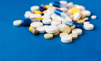 Heap of pills, tablets, capsules on blue background. Drug prescription for treatment medication health care concept wth copy space.
