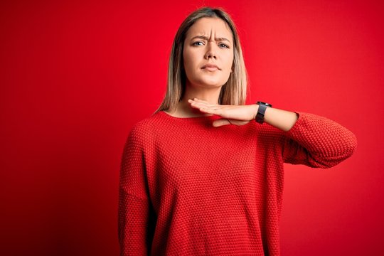 Young beautiful blonde woman wearing casual sweater over red isolated background cutting throat with hand as knife, threaten aggression with furious violence