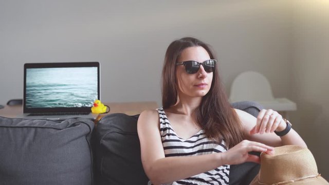 Sad woman in summer hat and sunglasses unhappily sitting on the sofa. Covid-19 summer lockdown 