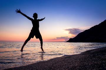 Fototapeta premium Backlit boy silhouette jumping with joy over the water on a beach of Cabo de Gata Natural Park, Almeria.