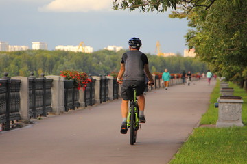 One cyclist men in sportsewar with helmet rides on a bicycle on asphalted road Nagatinskaya quayside of the Moscow River on a summer day, back view. Outdoor active vacation of Muscovites