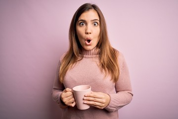 Young blonde woman drinking a cup of coffee over pink isolated background scared in shock with a surprise face, afraid and excited with fear expression