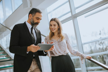 Senior business man and his young female colleague standing in office with digital tablet