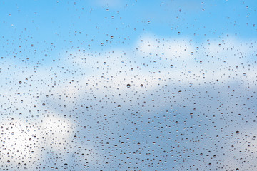 Water drops on the glass of a window with a blue sky and clouds in the background