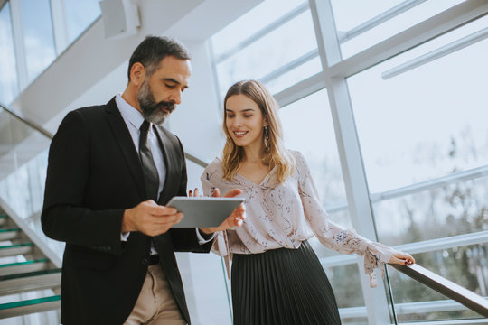 Senior Business Man And His Young Female Colleague Standing In Office With Digital Tablet