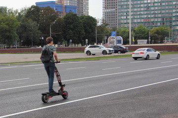 A guy on an electric scooter fast rides on a highway in the city, urban road safety kids
