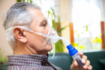 Senior man using medical equipment for inhalation with respiratory mask, nebulizer