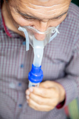 Fototapeta premium Senior man using medical equipment for inhalation with respiratory mask, nebulizer