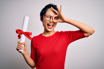 Beautiful chinese student woman wearing glasses holding university graduated diploma degree with happy face smiling doing ok sign with hand on eye looking through fingers