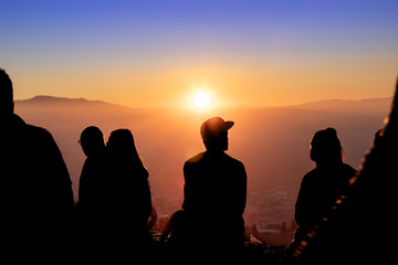 Group of people backlit during a sunset with the sun and mountains in the background. Viewpoint of San Miguel Alto, Granada.