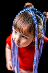 A little girl on a black background with Afro-pigtails, artificial plaited in elastic bands and put on