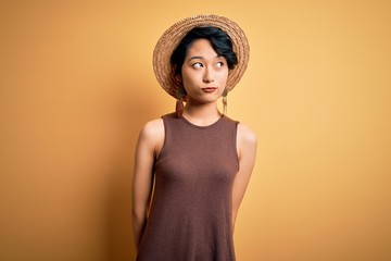 Young beautiful asian girl wearing casual t-shirt and hat over isolated yellow background smiling looking to the side and staring away thinking.