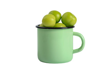 Green plums in an iron mug isolated on a white background. Close-up. Top view.