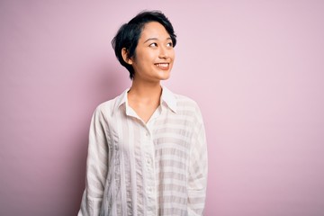 Fototapeta premium Young beautiful asian girl wearing casual shirt standing over isolated pink background looking away to side with smile on face, natural expression. Laughing confident.