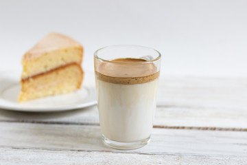 Dalgona coffee in glass cup on white background with honey cream cake piece