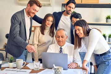 Group of business workers smiling happy and confident. One of them sitting and partners standing around. Working together with smile on face looking at the laptop at the office