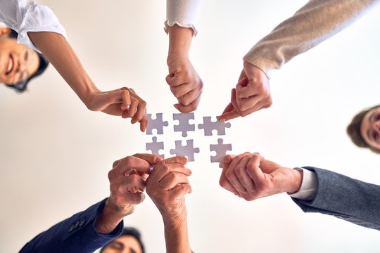 Group of business workers with hands together connecting pieces of puzzle at the office