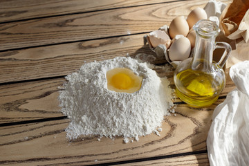 Dough preparation: flour, eggs, olive oil on a wooden table