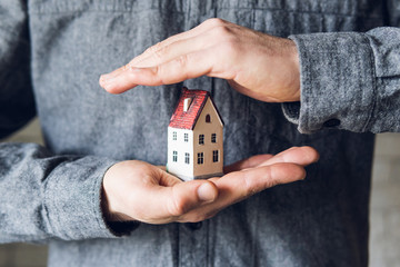 Male hands holding and protecting small toy house. Conceptual image of insurance and staying home...