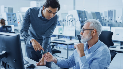 Modern Factory Office: Indian Project Manager Talks to Caucasian Senior Engineer who Working on...