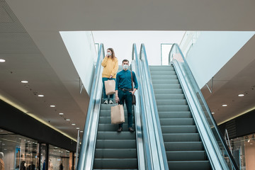 young man in a protective mask standing on an escalator in a shopping center