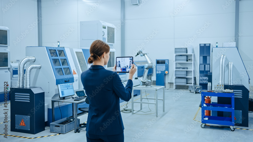 Poster Modern Factory: Female Engineer Uses Digital Tablet Computer with Augmented Reality Software to Visualize Workshop for Room Mapping, Floor Layout. Facility with High-Tech CNC Machinery and Robot Arm