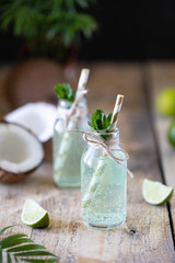 Two bottles of coconut water with mint and lime on a wooden table. Vegetarian drink. Mojito. Copy...