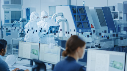 In Clean Workshop: Professional Workers in Coveralls and Masks Use Laptop and Talk. Inside Factory Office: Female Electronics Engineer Works on Computer, Screen Shows Printed Circuit Board 3D Design