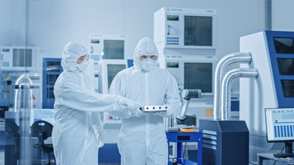 Naklejka premium Sterile Modern Factory: Professionals in Coveralls, Masks Walk Through Workshop and Talk. Medical Electronics Manufacturing Laboratory with High Tech CNC Machinery, Robot Arm Production Line.
