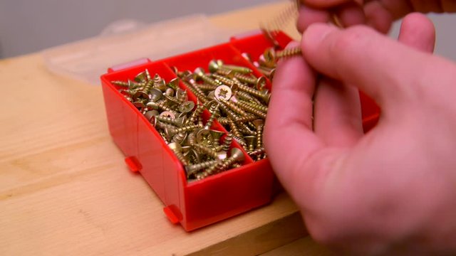 Close-up. A man opens a plastic box with the screws.