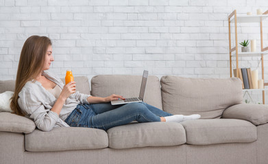 Young woman working on laptop and drinking fresh orange detox