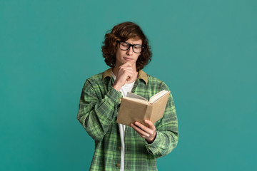 Back to school. Industrious student in glasses reading interesting book on turquoise background