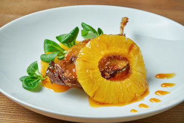 Appetizing duck leg confit with pineapple and spinach in a white plate on a wooden background. Restaurant serving from the chef