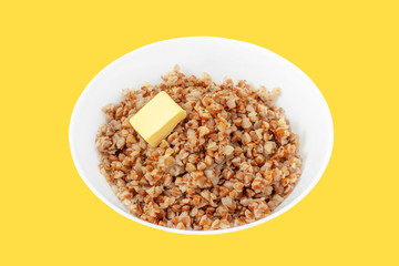 Deep white plate with boiled buckwheat and a piece of butter close-up.