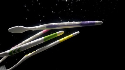 Super slow motion white toothbrushes falling into the water scattering bubbles on a black background, close up. - Powered by Adobe