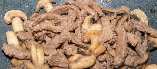 Homemade cooking veal and mushrooms in frying pan. Close-up macro photo of julian chopped meat. Smoke of meat cooked in its own juice comes out.