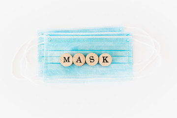 Word mask written with wooden blocks with black letters laying on protective surgical masks, flat lay concept