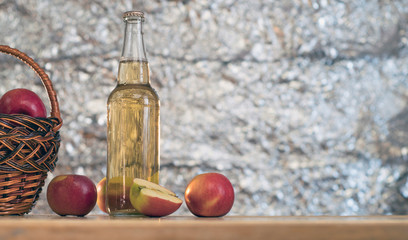 Basket with red fresh apples and a bottle of cider on a wooden table.